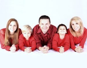 Cheesy family photo: family of four dressed in red behind fake white background.