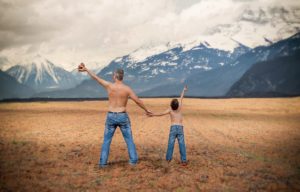 Father and son bare chested facing the mountains.